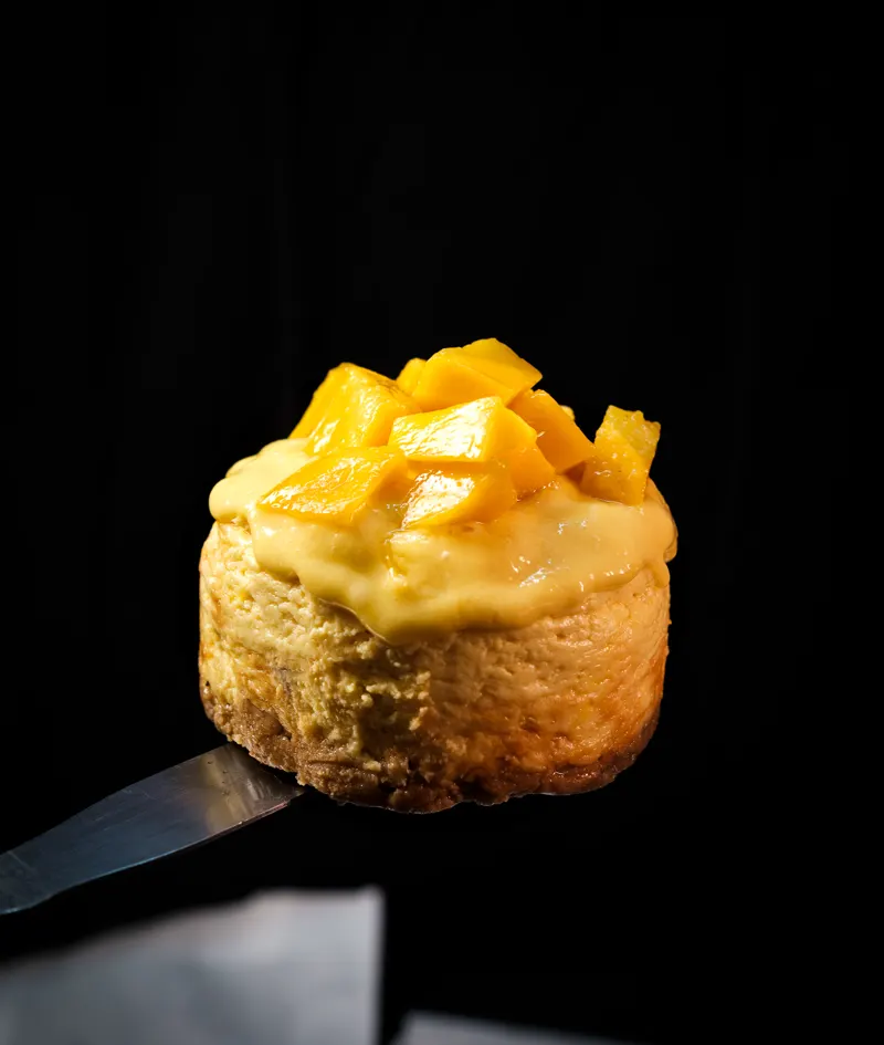 Cheesecake de mango sobre espátula con fondo oscuro