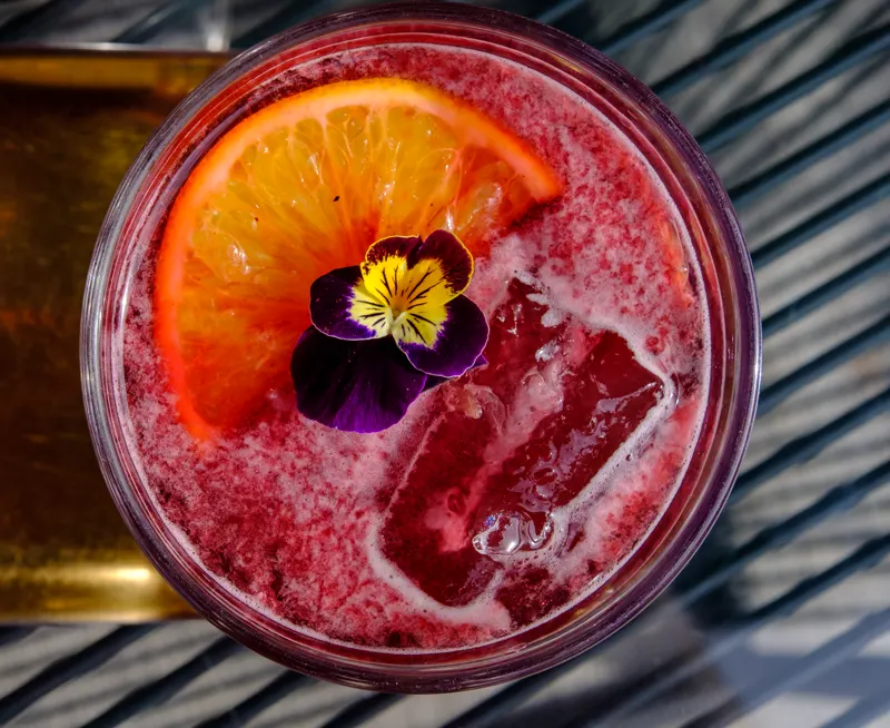 Bebida roja con naranja y flor comestible vista desde arriba