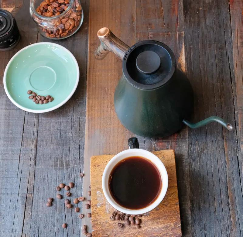Tetera, taza de café y granos sobre madera