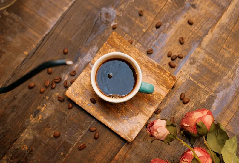 Taza de café sobre madera, rodeada de granos y rosas